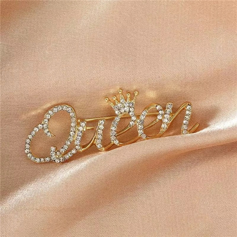 Goldinschrift „Queen“ mit einer Krone – Brosche mit Zirkonia
