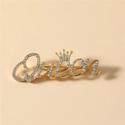 Goldinschrift „Queen“ mit einer Krone – Brosche mit Zirkonia