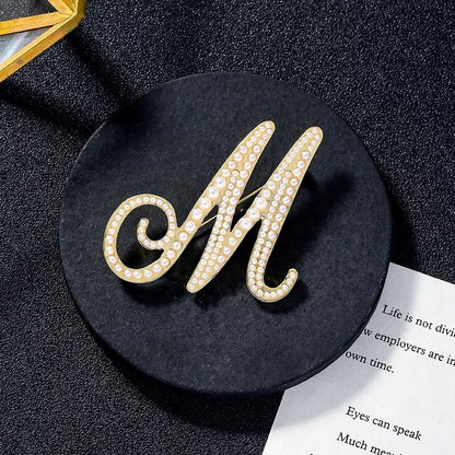 Goldene Brosche mit dem Buchstaben M und Perlen