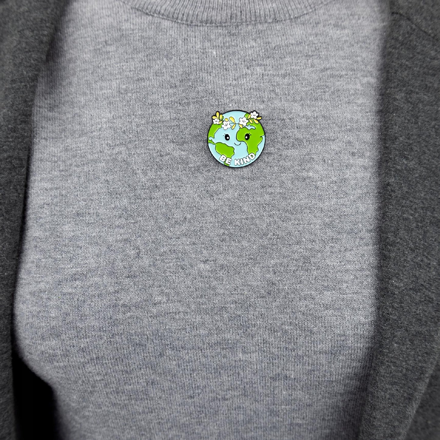 Ökologische Anstecknadel in Form des Planeten Erde mit einem Kranz und dem Slogan „Be Kind“